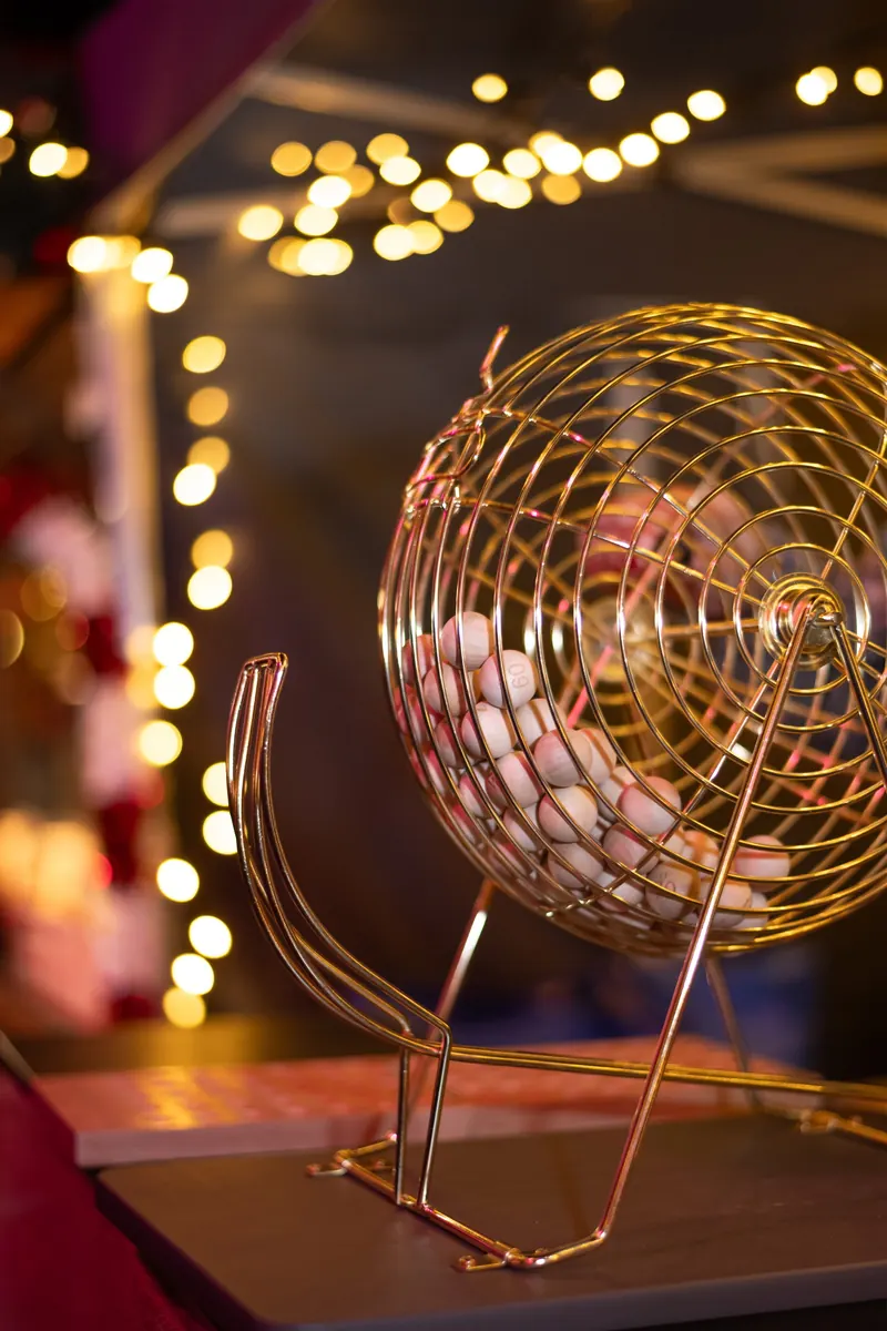 Goldene Bingotrommel mit nummerierten Kugeln vor einer Lichterkette