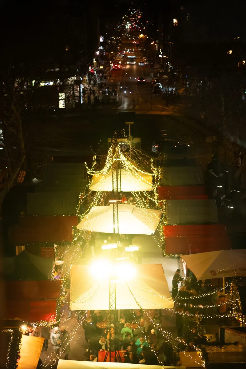 Blick von oben auf die beleuchteten Hütten und Lichterketten des Markts bei Nacht