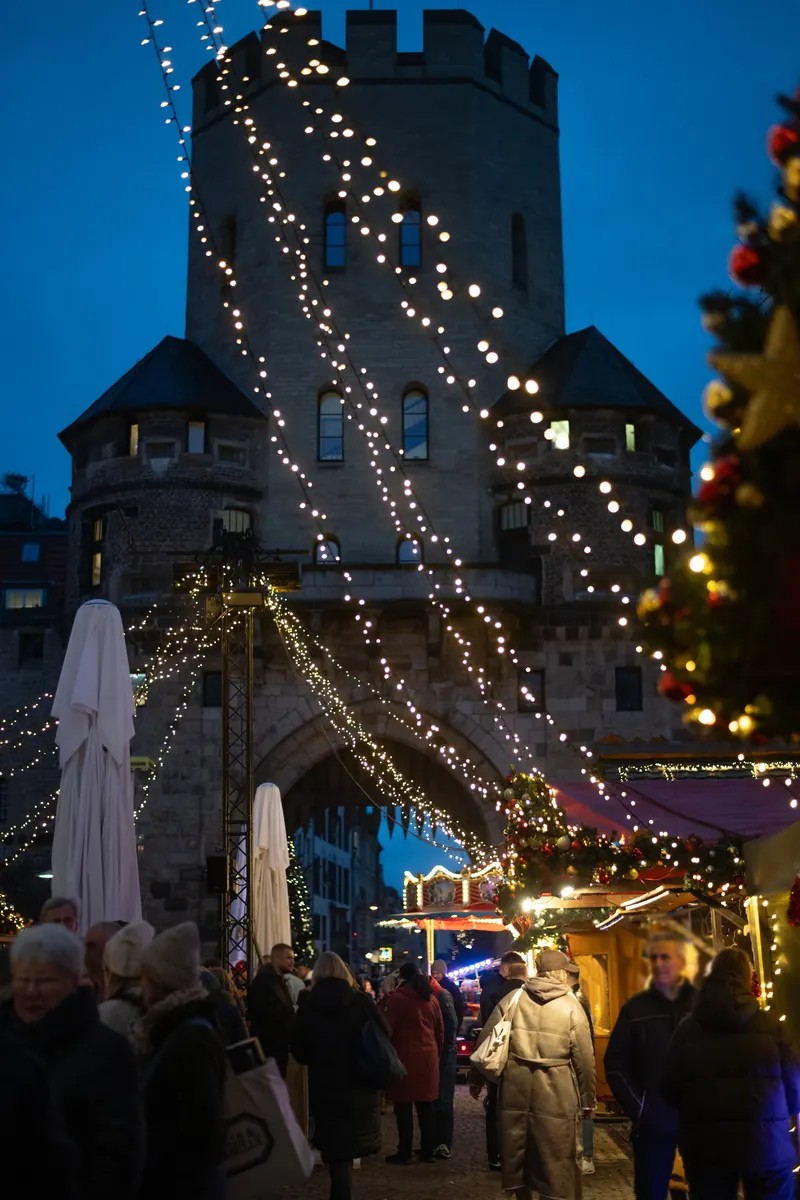 Lichterketten über dem Markt vor dem Torbogen der Severinstorburg zur blauen Stunde