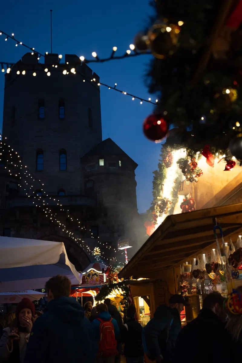 Marktstände und Besucher in der Dämmerung, dahinter der Turm der Severinstorburg